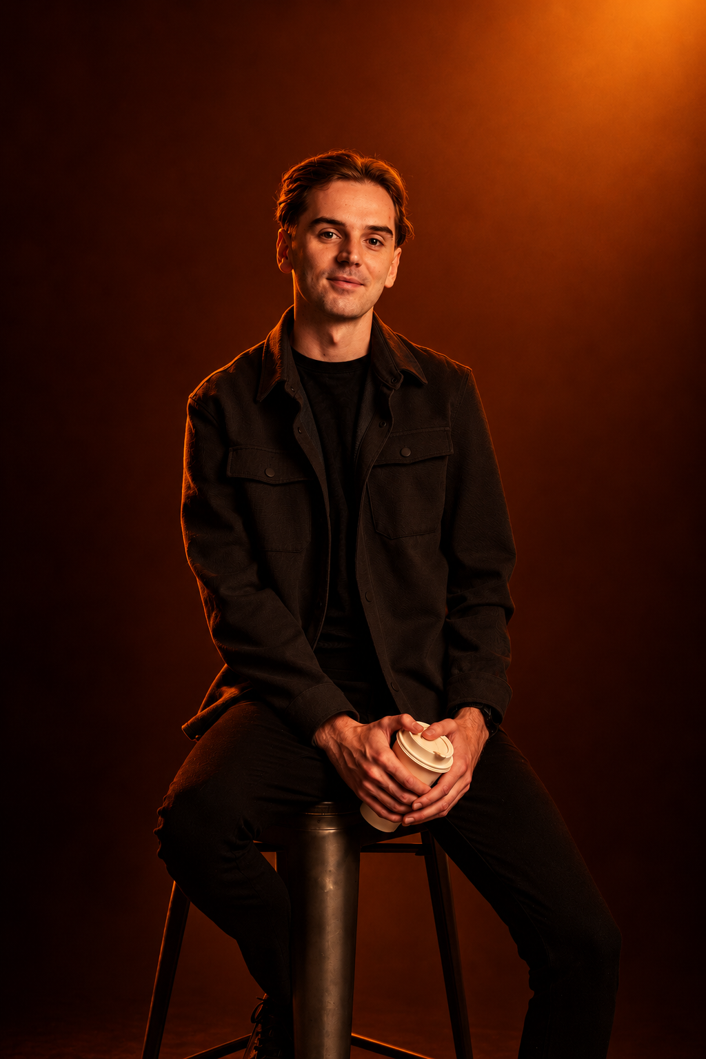 Portrait of Aaron seated against a warm orange background