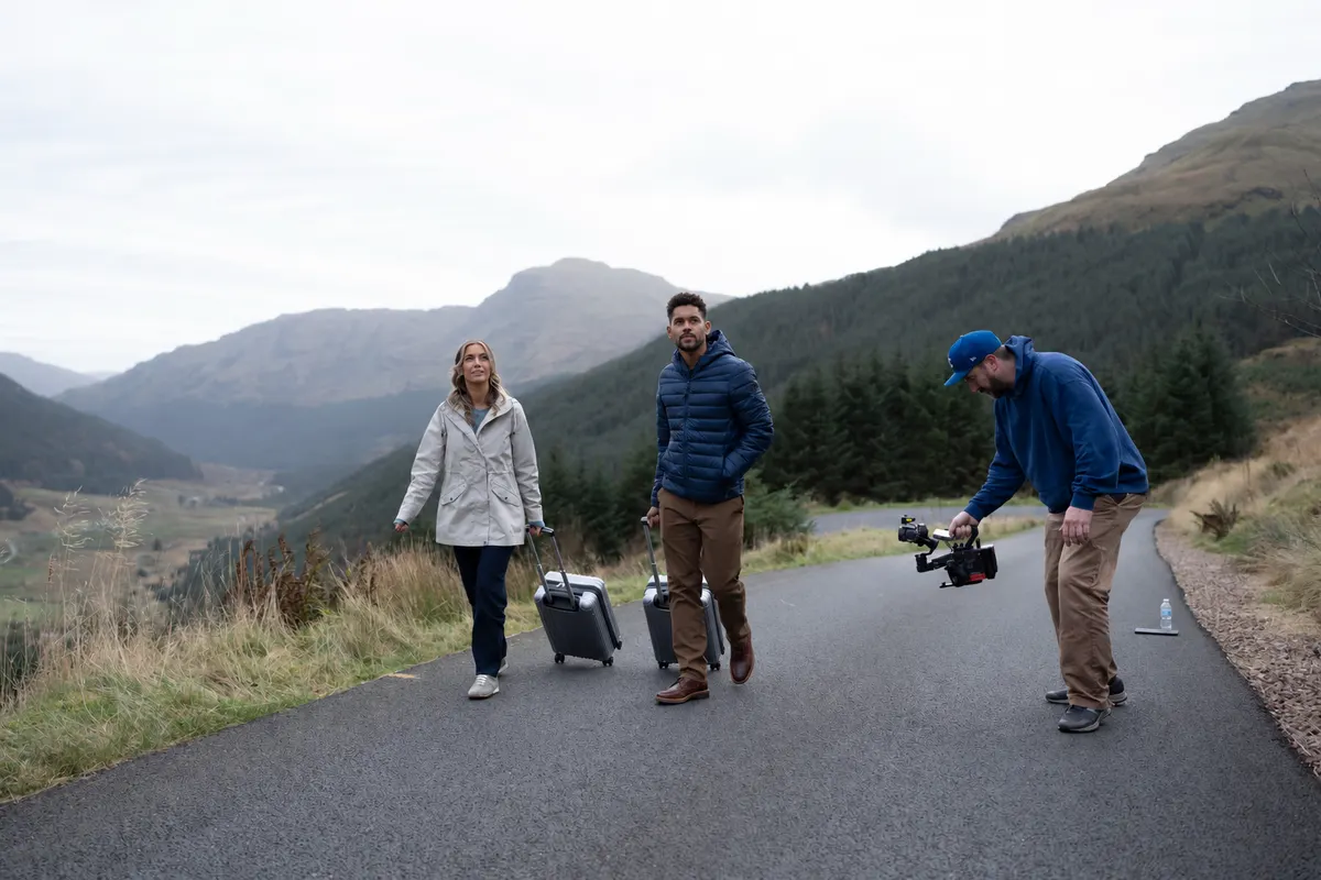 Camera operator filming two travellers with suitcases on a Scottish road